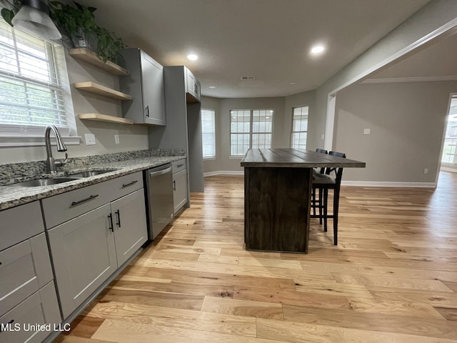 kitchen with a sink, dishwasher, light wood-style flooring, baseboards, and a kitchen bar