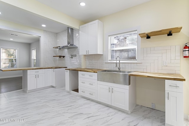 kitchen featuring white cabinetry, sink, wooden counters, and wall chimney range hood