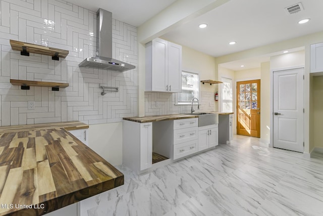 kitchen with butcher block counters, white cabinetry, and wall chimney range hood