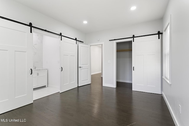 unfurnished bedroom with ensuite bathroom, a barn door, dark wood-type flooring, and a closet