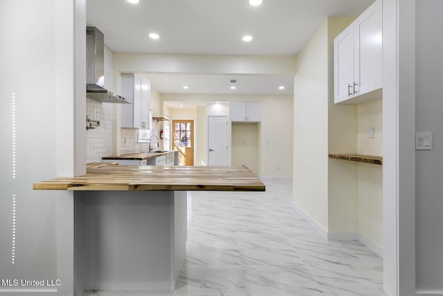 kitchen featuring kitchen peninsula, a kitchen breakfast bar, sink, wall chimney range hood, and white cabinetry