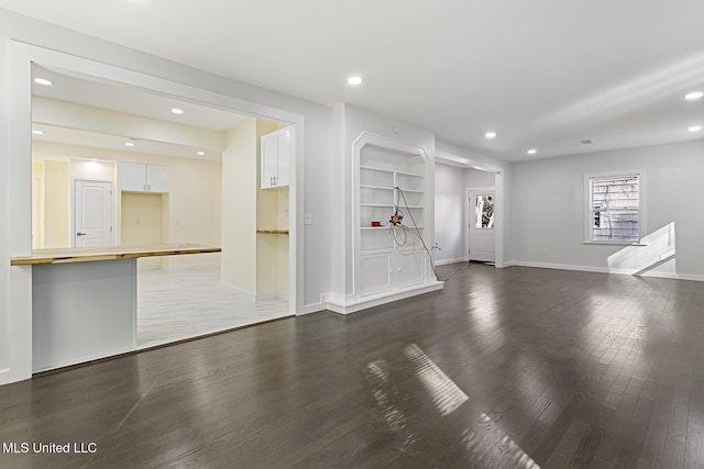 unfurnished living room with built in shelves and dark wood-type flooring