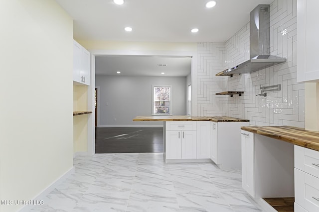 kitchen featuring wooden counters, decorative backsplash, white cabinetry, and wall chimney range hood