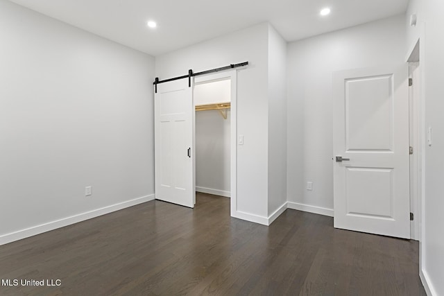 unfurnished bedroom featuring a barn door, a closet, dark hardwood / wood-style flooring, and a spacious closet