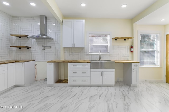 kitchen with wall chimney exhaust hood, a wealth of natural light, white cabinets, and wood counters