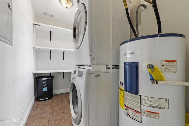 washroom with stacked washer and dryer, visible vents, electric water heater, dark tile patterned flooring, and laundry area