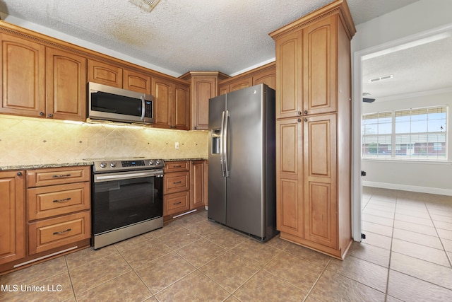 kitchen with decorative backsplash, appliances with stainless steel finishes, light stone countertops, tile patterned flooring, and a textured ceiling