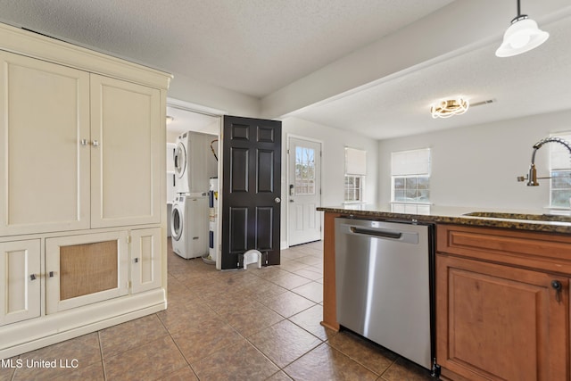 kitchen featuring stacked washer / dryer, a sink, a textured ceiling, dark tile patterned flooring, and dishwasher