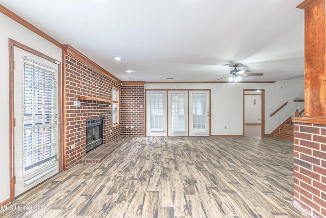 unfurnished living room with ceiling fan, ornamental molding, wood-type flooring, and a brick fireplace