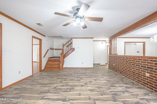 basement with ceiling fan with notable chandelier, hardwood / wood-style flooring, crown molding, and brick wall