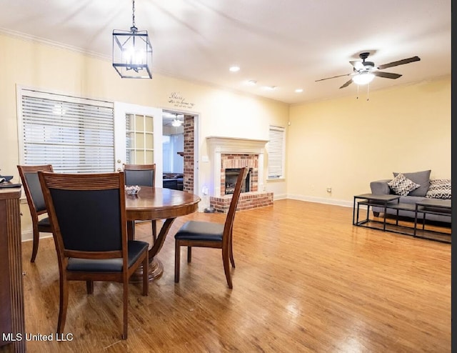 dining area with wood-type flooring, a brick fireplace, crown molding, and ceiling fan