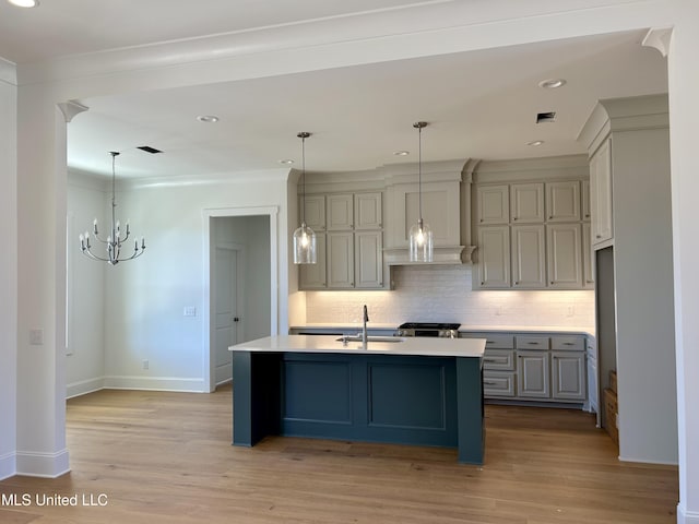 kitchen with gray cabinets, light countertops, backsplash, a kitchen island with sink, and a sink