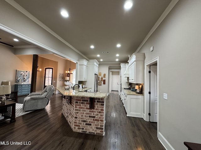 kitchen with a kitchen bar, white cabinetry, light stone counters, ornamental molding, and kitchen peninsula