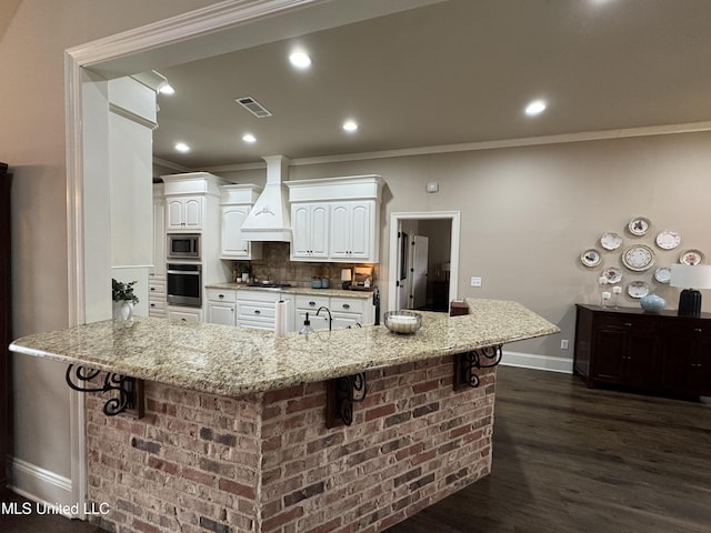 kitchen featuring a breakfast bar area, custom exhaust hood, light stone counters, appliances with stainless steel finishes, and white cabinets