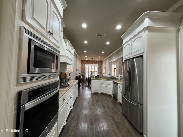 kitchen with appliances with stainless steel finishes, pendant lighting, white cabinetry, light stone counters, and kitchen peninsula