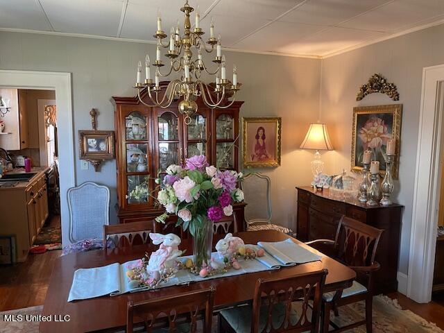 dining room featuring sink, dark wood-type flooring, a notable chandelier, and ornamental molding