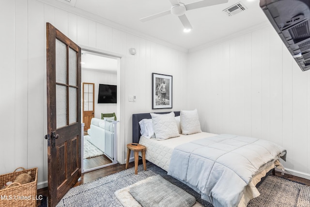 bedroom with hardwood / wood-style floors, ornamental molding, ceiling fan, and wooden walls