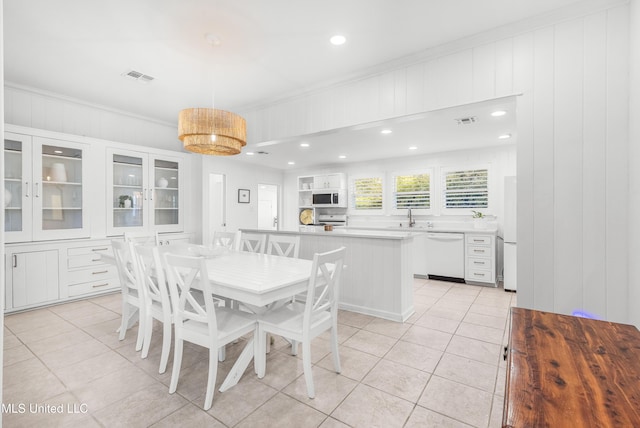 dining space with crown molding, sink, light tile patterned floors, and wood walls