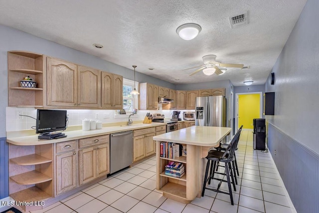 kitchen with ceiling fan, hanging light fixtures, a kitchen breakfast bar, stainless steel appliances, and light brown cabinetry