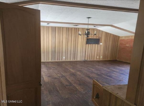 interior space featuring a textured ceiling, lofted ceiling, dark hardwood / wood-style floors, and wooden walls