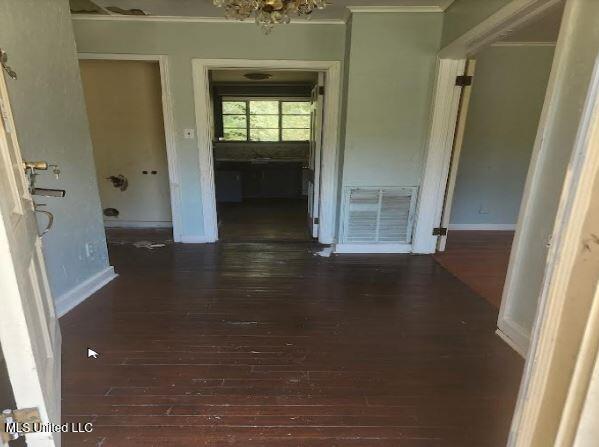 hallway with crown molding, dark wood-type flooring, and an inviting chandelier