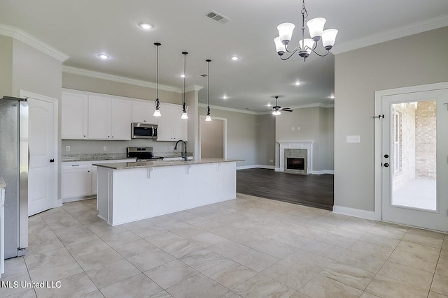 kitchen featuring light stone countertops, appliances with stainless steel finishes, pendant lighting, white cabinetry, and an island with sink