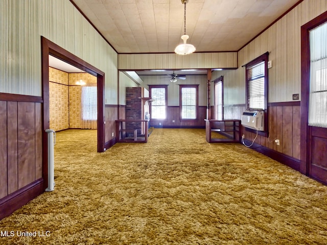 unfurnished dining area featuring ornamental molding, carpet, a ceiling fan, and wood walls