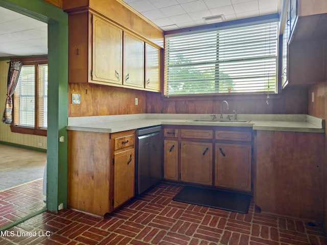 kitchen featuring wooden walls, a sink, brick floor, light countertops, and stainless steel dishwasher