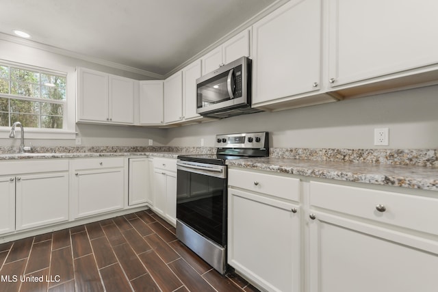 kitchen with appliances with stainless steel finishes, wood tiled floor, white cabinets, and a sink