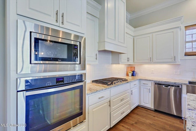 kitchen with crown molding, appliances with stainless steel finishes, light hardwood / wood-style floors, white cabinets, and decorative backsplash