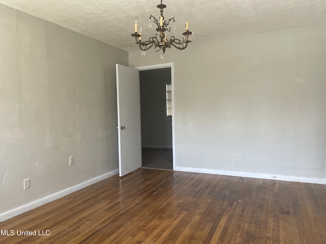 empty room featuring a chandelier, hardwood / wood-style flooring, baseboards, and a textured ceiling