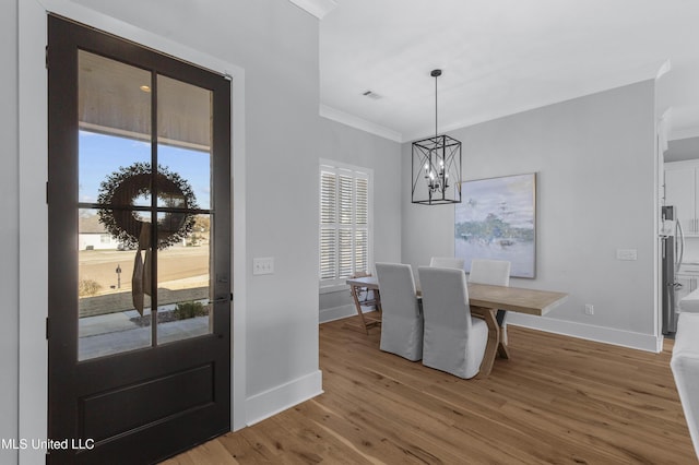 dining space featuring wood-type flooring, crown molding, and a notable chandelier