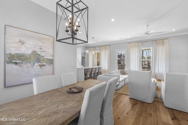 dining space with crown molding, light hardwood / wood-style flooring, ceiling fan with notable chandelier, and sink