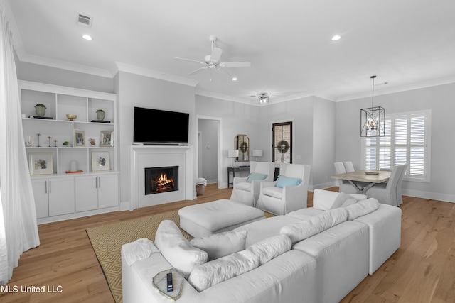 living room with crown molding, ceiling fan with notable chandelier, and light wood-type flooring