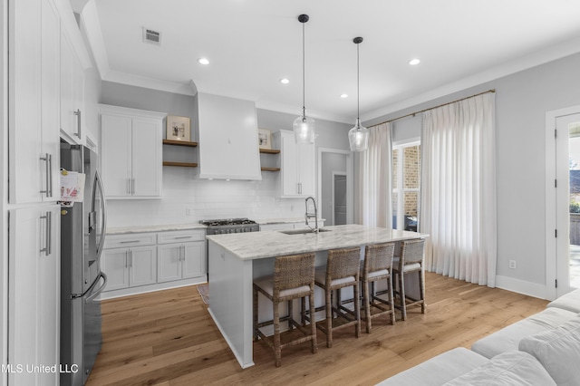 kitchen with pendant lighting, a center island with sink, light hardwood / wood-style flooring, white cabinetry, and stainless steel refrigerator