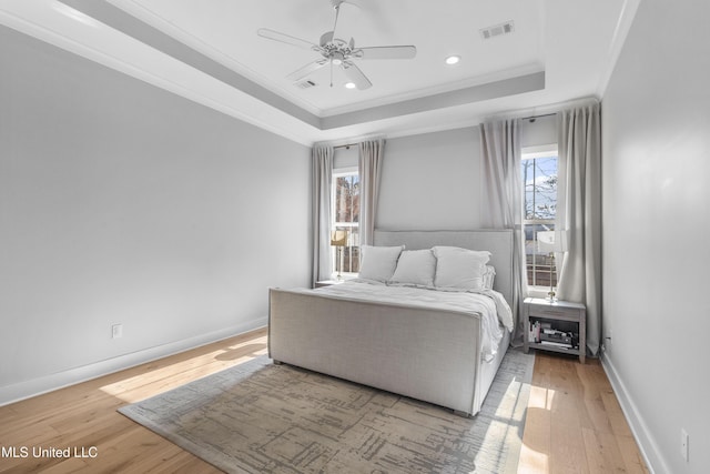 bedroom with wood-type flooring, a raised ceiling, ceiling fan, and crown molding