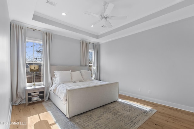 bedroom with ceiling fan, a raised ceiling, light wood-type flooring, and multiple windows