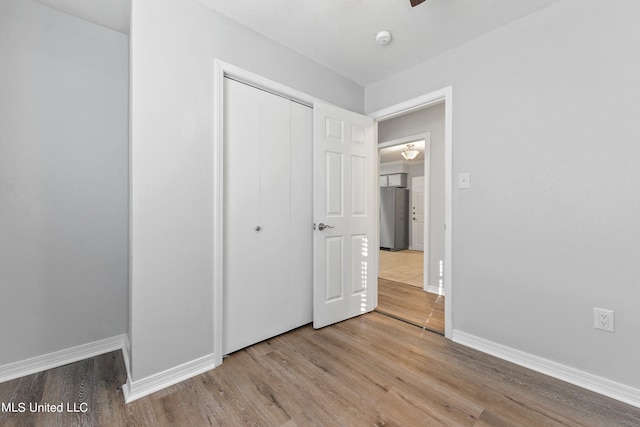 unfurnished bedroom with stainless steel fridge, light hardwood / wood-style flooring, and a closet