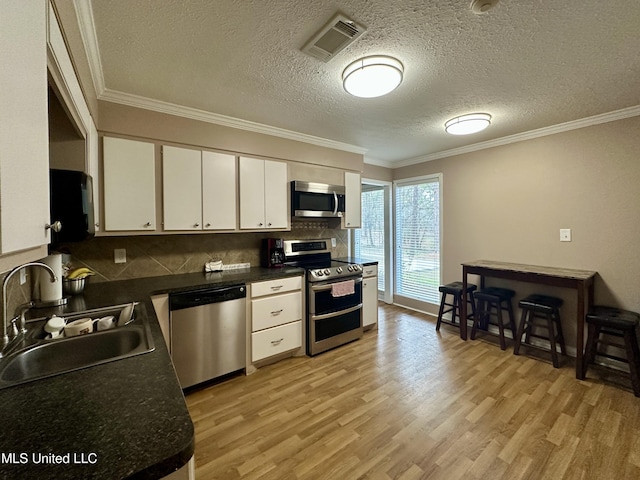 kitchen with appliances with stainless steel finishes, light hardwood / wood-style floors, crown molding, sink, and white cabinetry