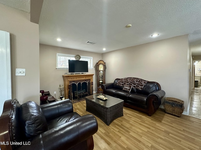 living room with a brick fireplace, a textured ceiling, and light hardwood / wood-style flooring