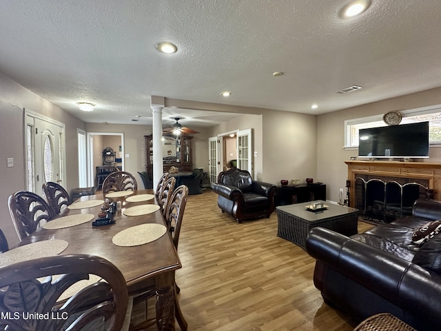 dining area with a textured ceiling, ornate columns, french doors, light wood-type flooring, and ceiling fan