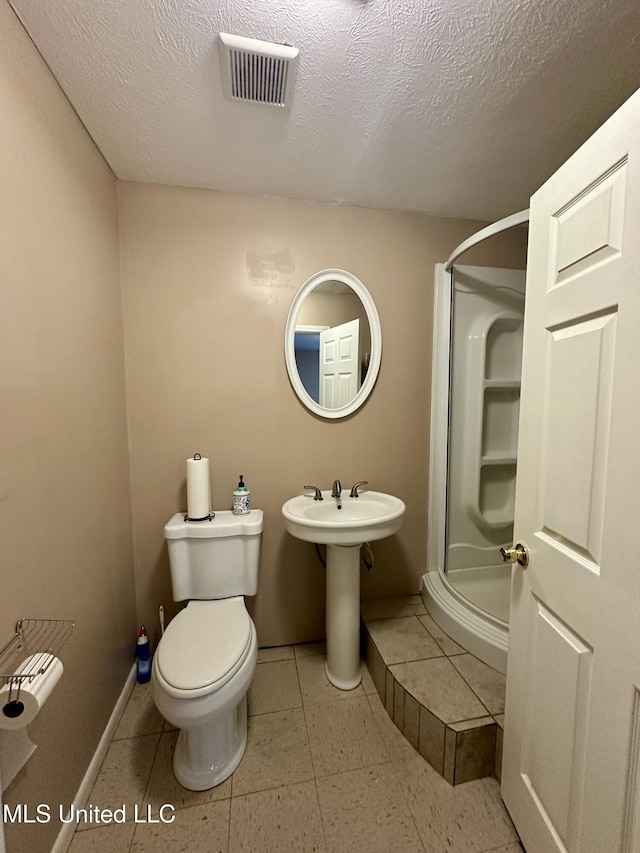 bathroom with toilet, a textured ceiling, tile patterned floors, and walk in shower