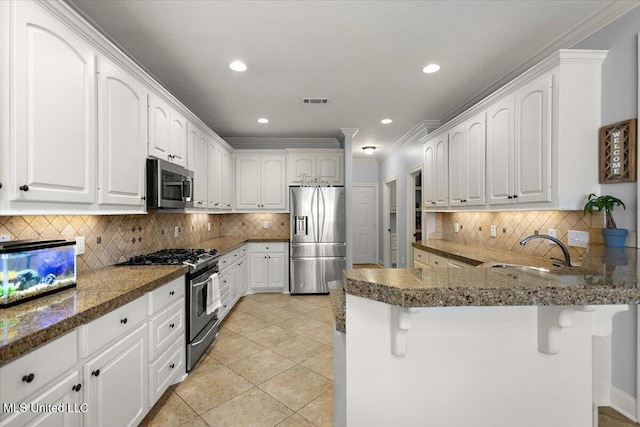 kitchen featuring a peninsula, light tile patterned flooring, a sink, stainless steel appliances, and a kitchen bar