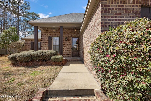 entrance to property featuring brick siding and roof with shingles