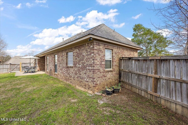 view of side of home featuring a patio, a yard, a fenced backyard, and brick siding