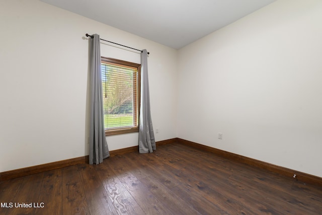 spare room with baseboards and dark wood-type flooring