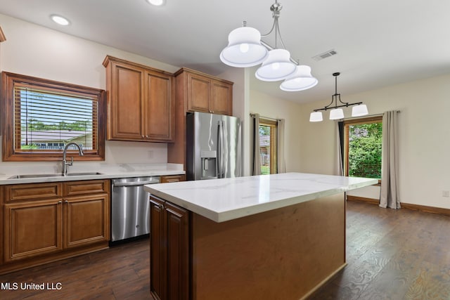kitchen featuring stainless steel appliances, a sink, brown cabinetry, dark wood finished floors, and hanging light fixtures