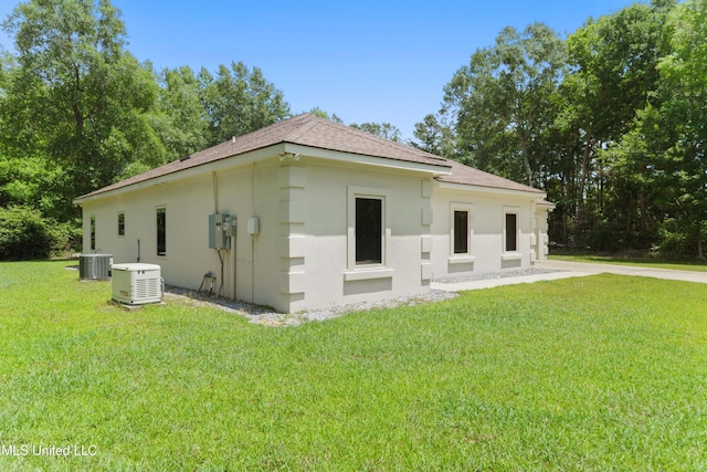 view of side of home featuring a shingled roof, central AC unit, a lawn, and stucco siding