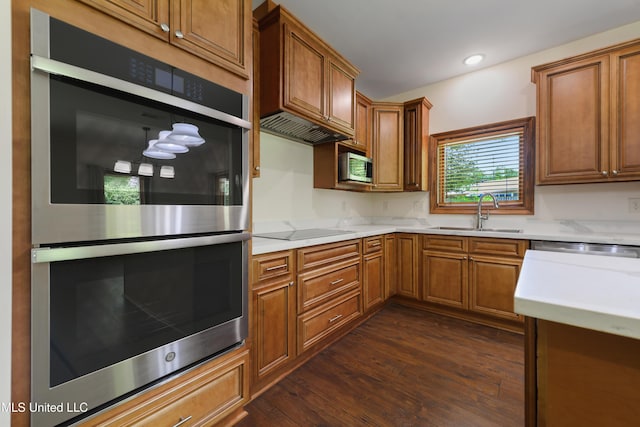 kitchen with stainless steel appliances, a sink, light countertops, dark wood-style floors, and brown cabinets