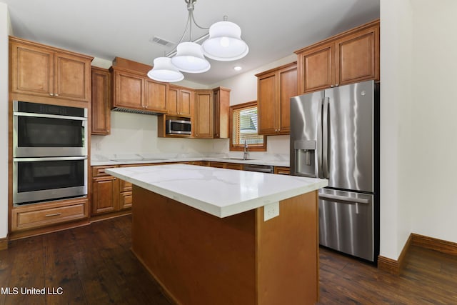 kitchen with stainless steel appliances, dark wood finished floors, brown cabinetry, a kitchen island, and a sink